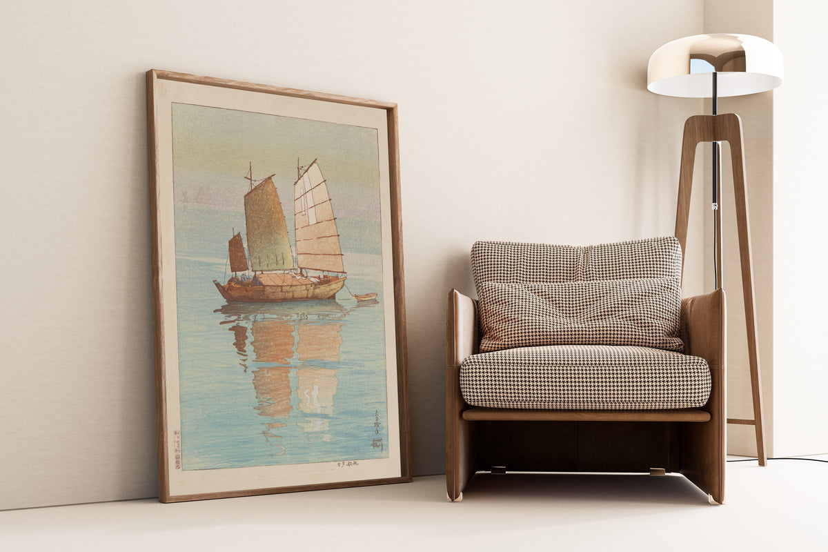 Framed art print of Sailing Boats, Evening Glow by Hiroshi Yoshida, leaning against a wall beside an armchair and a floor lamp