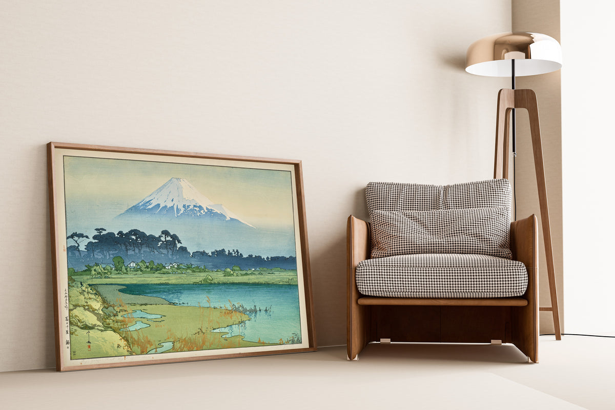 Framed art print of Sunrise by Hiroshi Yoshida, leaning against a wall beside an armchair and a floor lamp