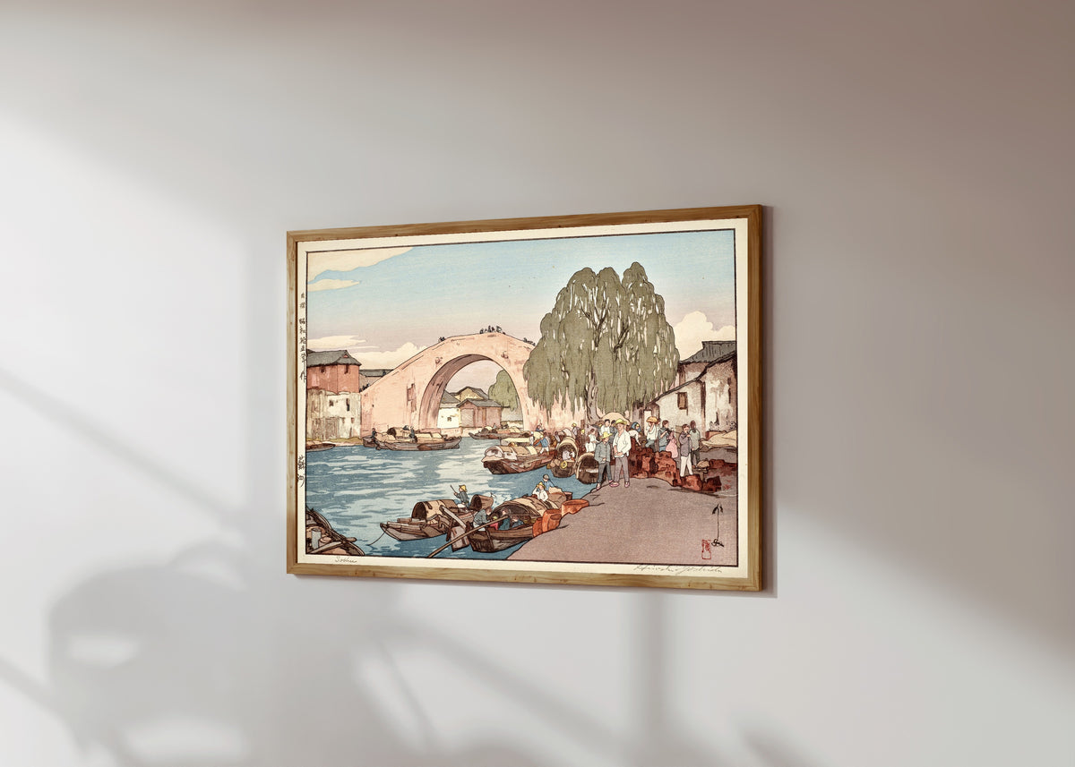 Framed art print of Suzhou by Hiroshi Yoshida, in a light wood frame on a sunlit white wall, seen at a slight angle