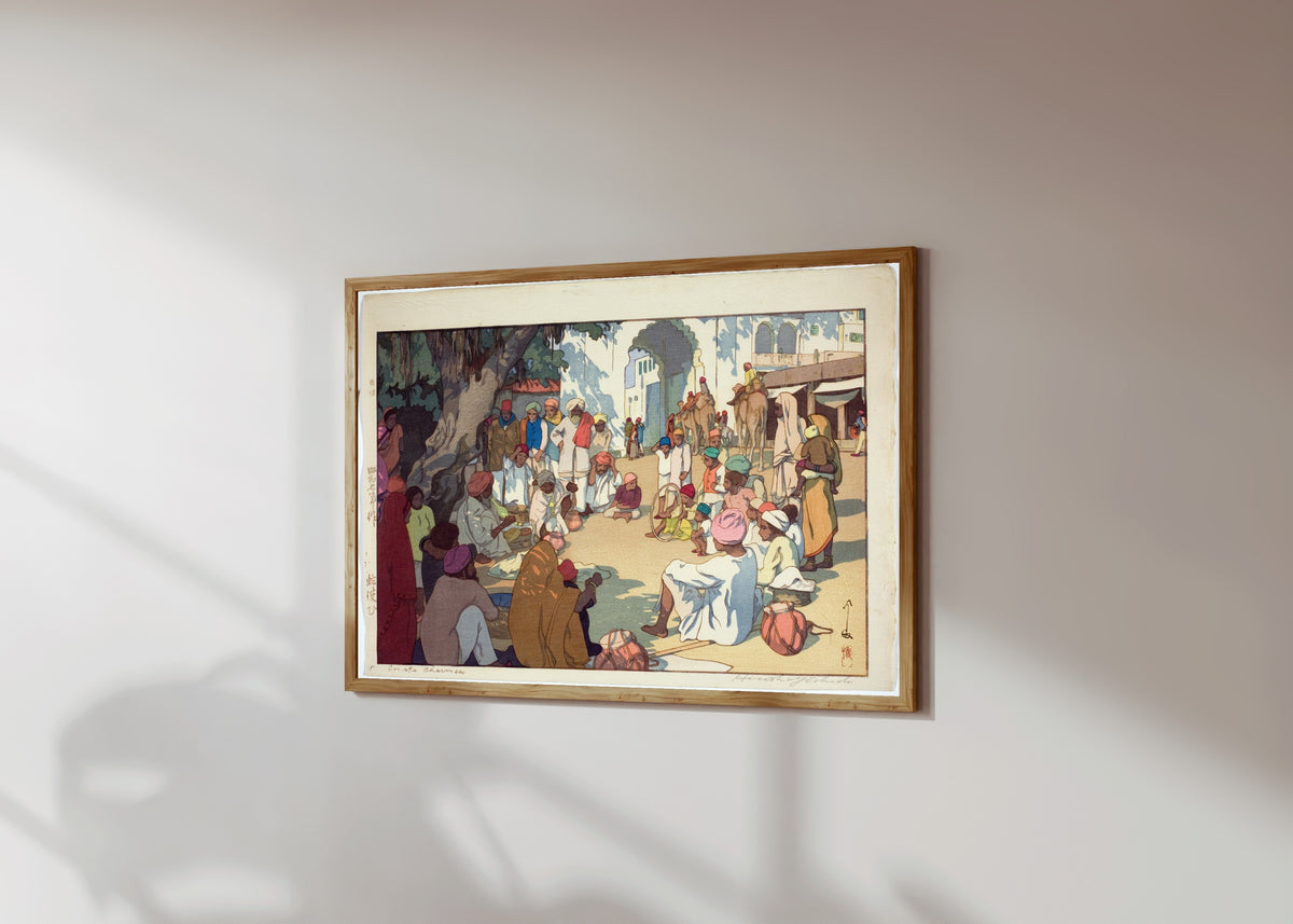 Framed art print of Snake Charmers by Hiroshi Yoshida, in a light wood frame on a sunlit white wall, seen at a slight angle