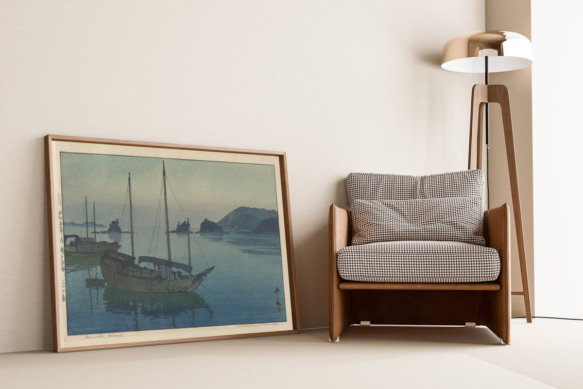 Framed art print of Three Little Islands by Hiroshi Yoshida, leaning against a wall beside an armchair and a floor lamp