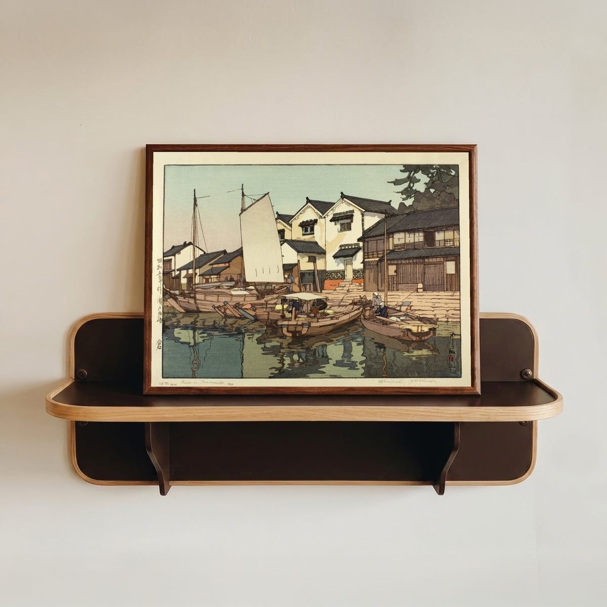 Framed art print of Tomonoura Warehouse by Hiroshi Yoshida, in a dark wood frame resting on a wall shelf