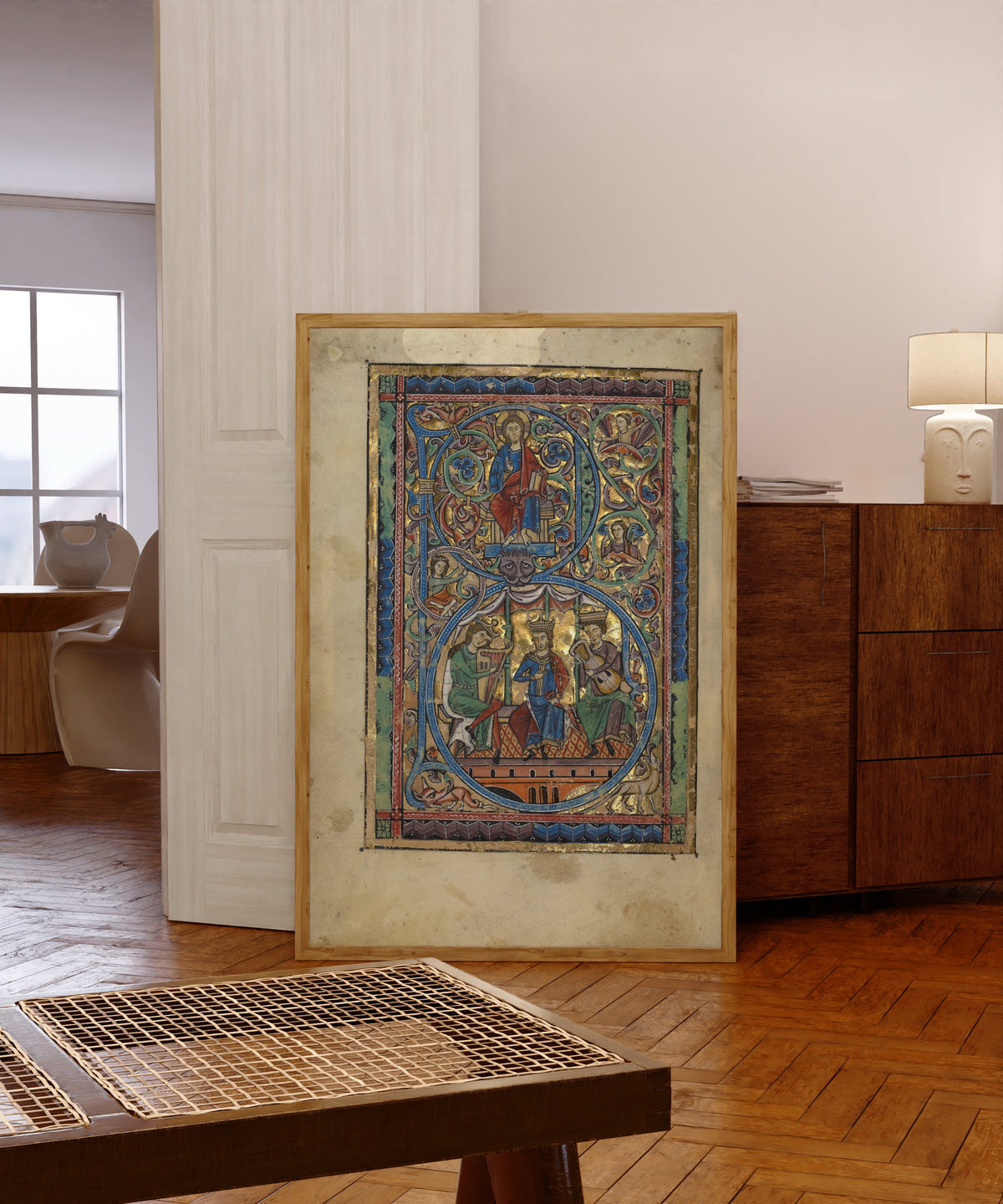 Framed art print of Initial B: Christ in Majesty and David with Musicians, in a light wood frame leaning in a warm room with a parquet floor