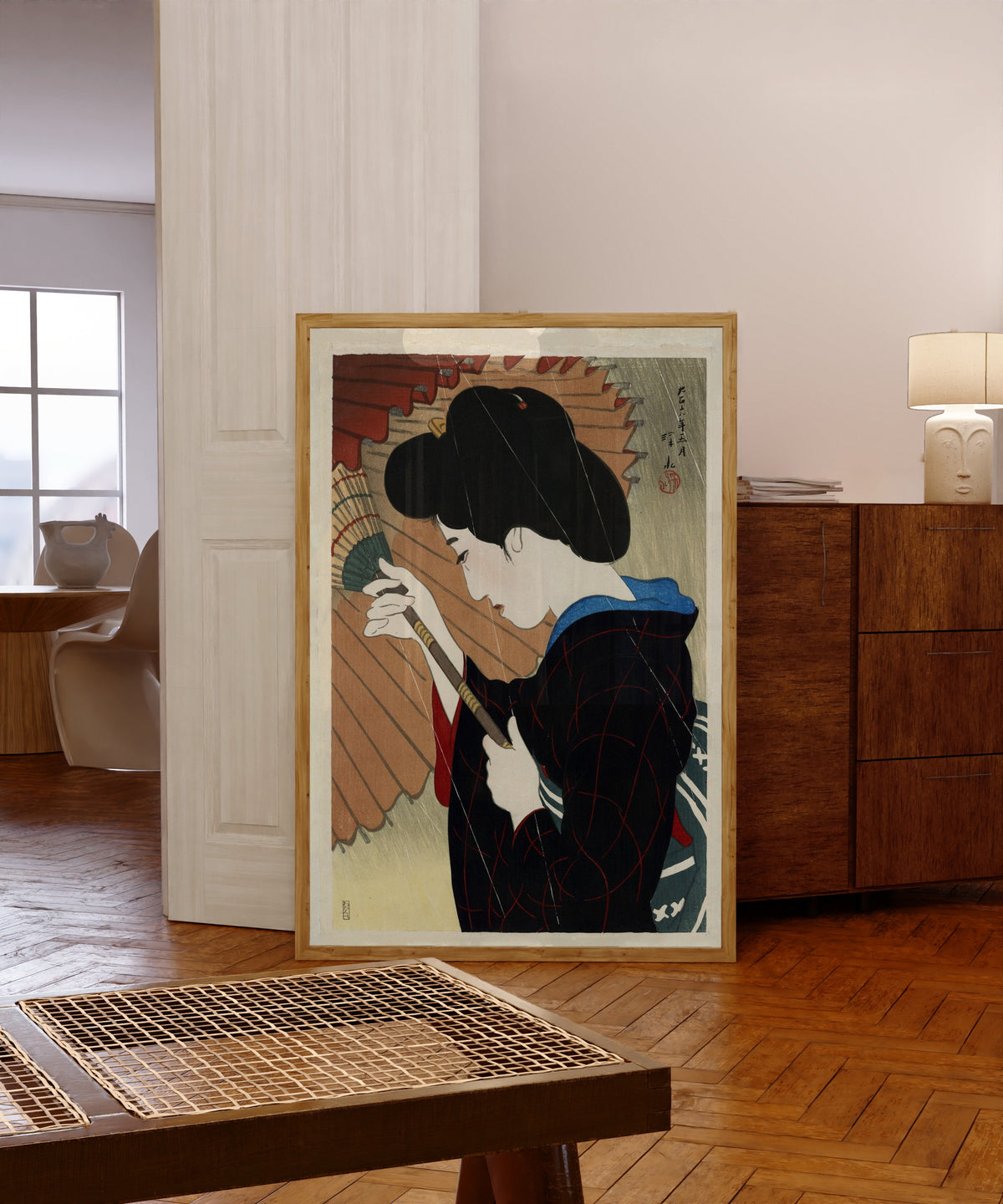 Framed art print of Passing Rain by Ito Shinsui, in a light wood frame leaning in a warm room with a parquet floor