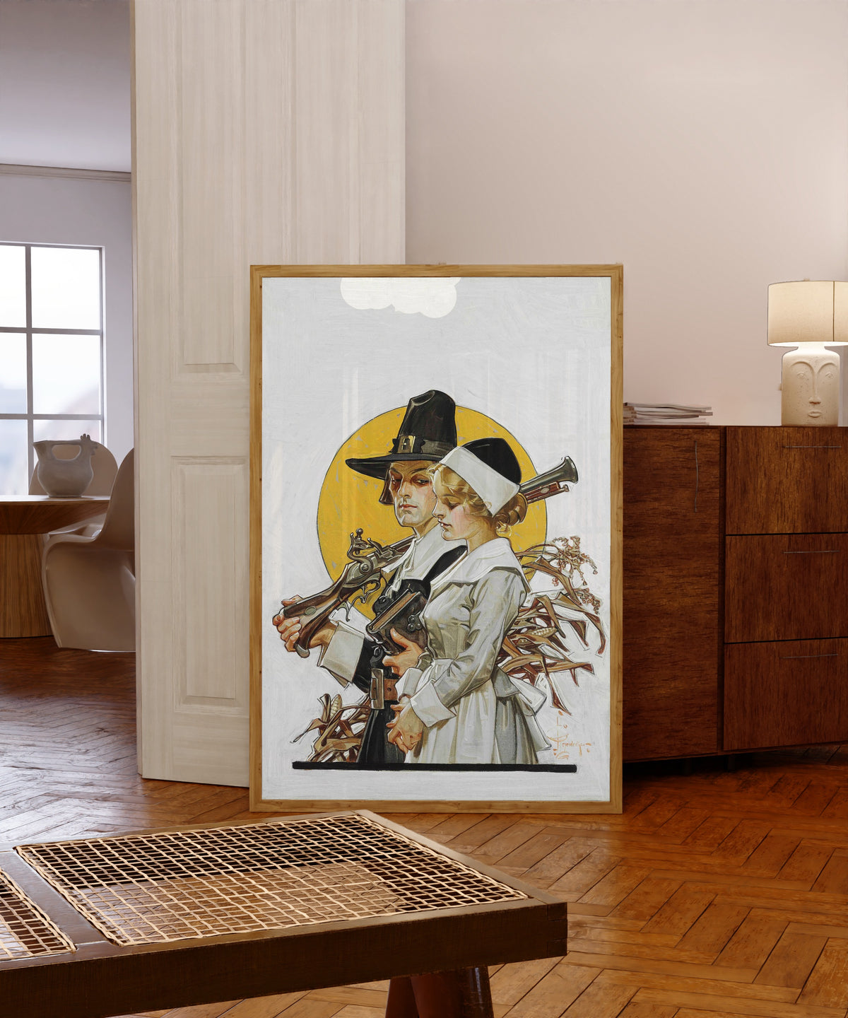 Framed art print of Giving Thanks (Thanksgiving Couple) by J.C. Leyendecker, in a light wood frame leaning in a warm room with a parquet floor
