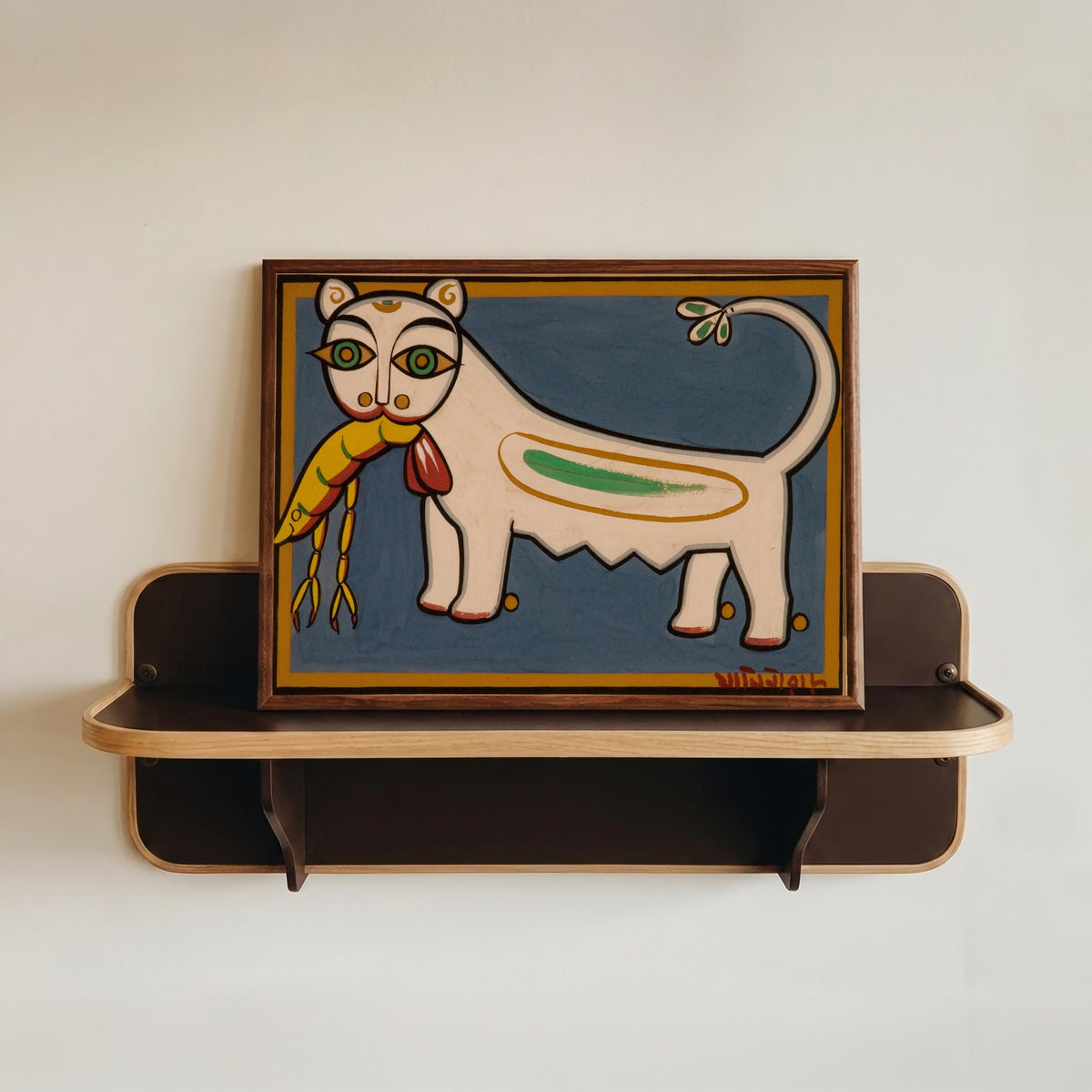 Framed art print of Cat and Shrimp by Jamini Roy, in a dark wood frame resting on a wall shelf