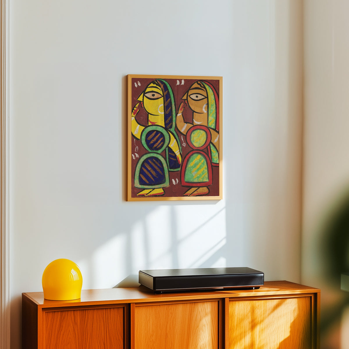 Framed art print of Untitled by Jamini Roy, in a light wood frame on a white wall above an orange sideboard