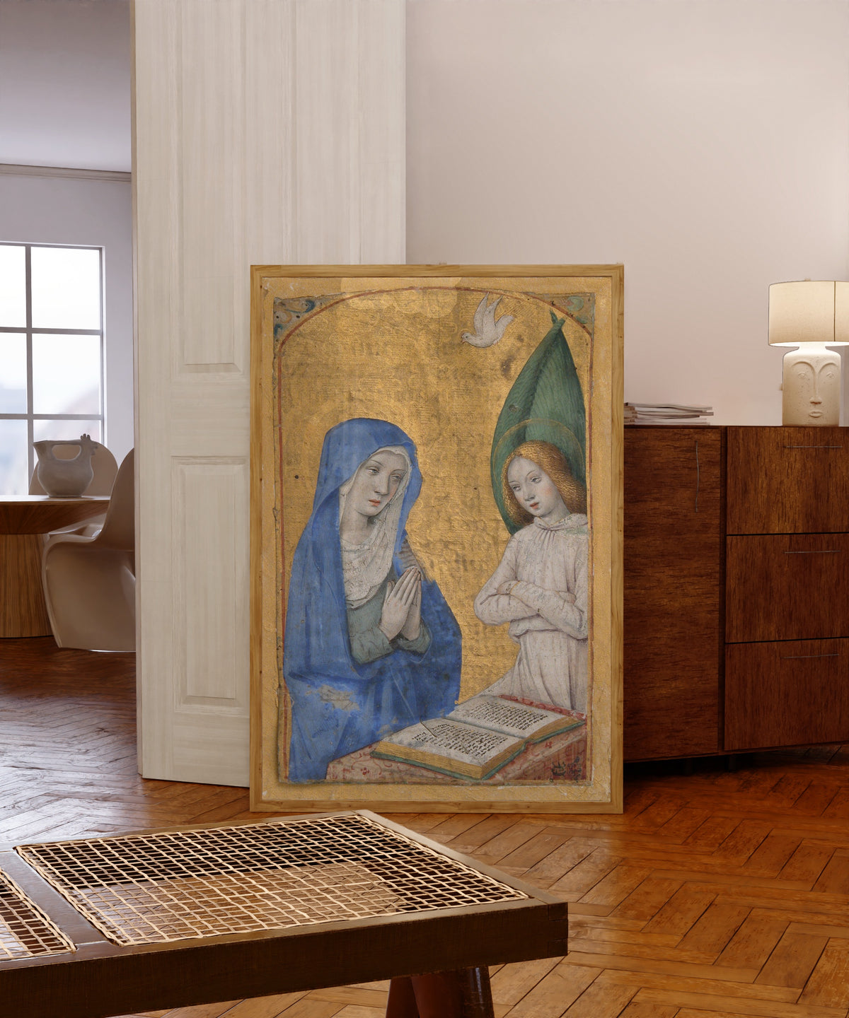 Framed art print of Book of Hours: The Annunciation by Jean Bourdichon, in a light wood frame leaning in a warm room with a parquet floor