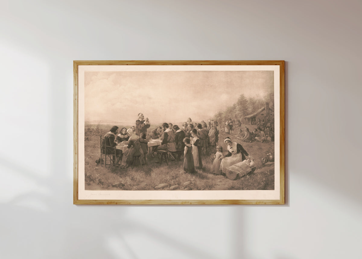 Framed art print of The First American Thanksgiving by Jennie Brownscombe, in a light wood frame on a sunlit white wall