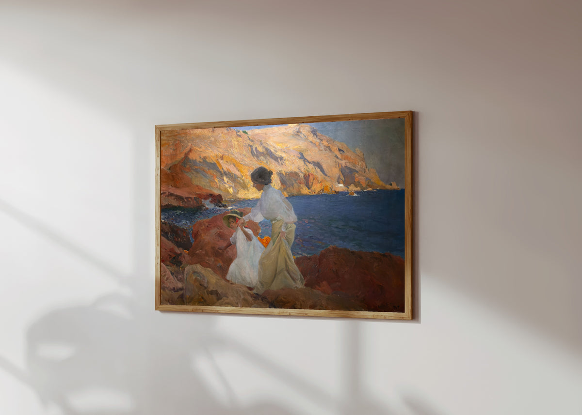 Framed art print of Clotilde and Elena on the Rocks, Jávea by Joaquín Sorolla, in a light wood frame on a sunlit white wall, seen at a slight angle