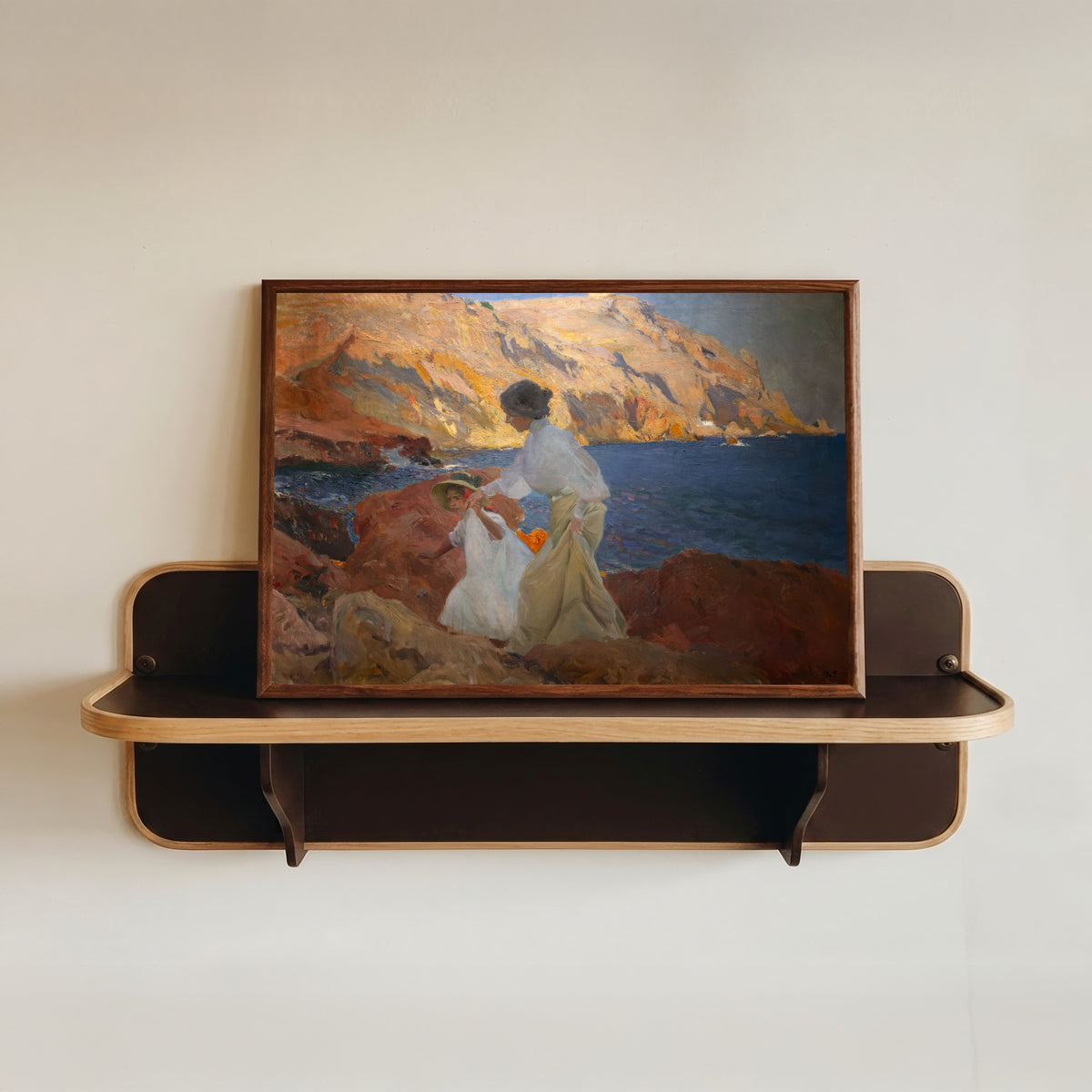 Framed art print of Clotilde and Elena on the Rocks, Jávea by Joaquín Sorolla, in a dark wood frame resting on a wall shelf