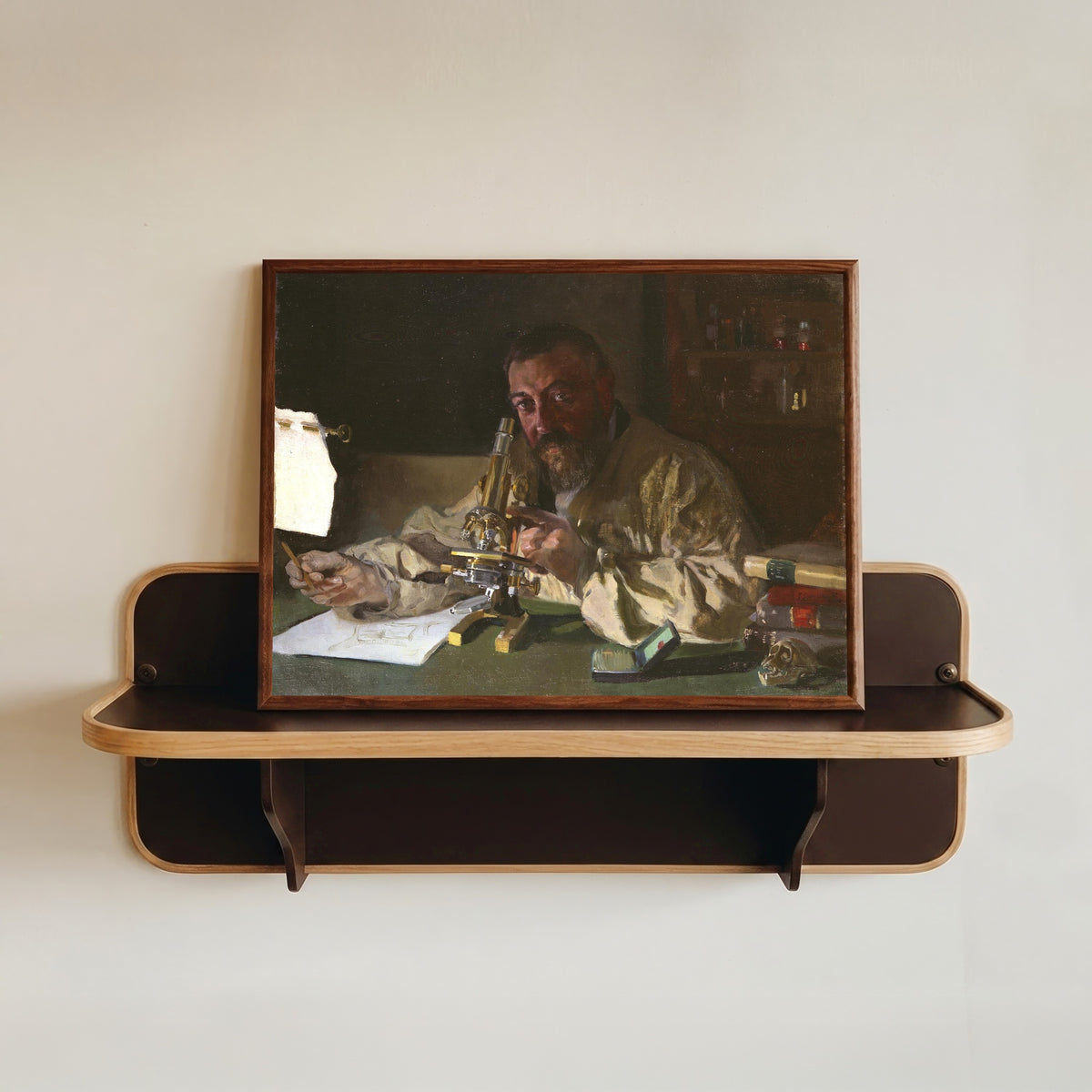 Framed art print of Dr. Simarro at the Microscope by Joaquín Sorolla, in a dark wood frame resting on a wall shelf