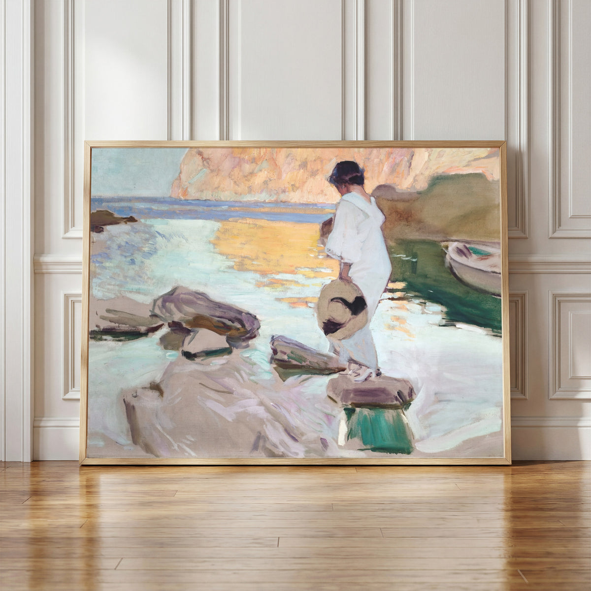 Framed art print of Elena at Cala de San Vicente by Joaquín Sorolla, in a light wood frame leaning against a panelled white wall