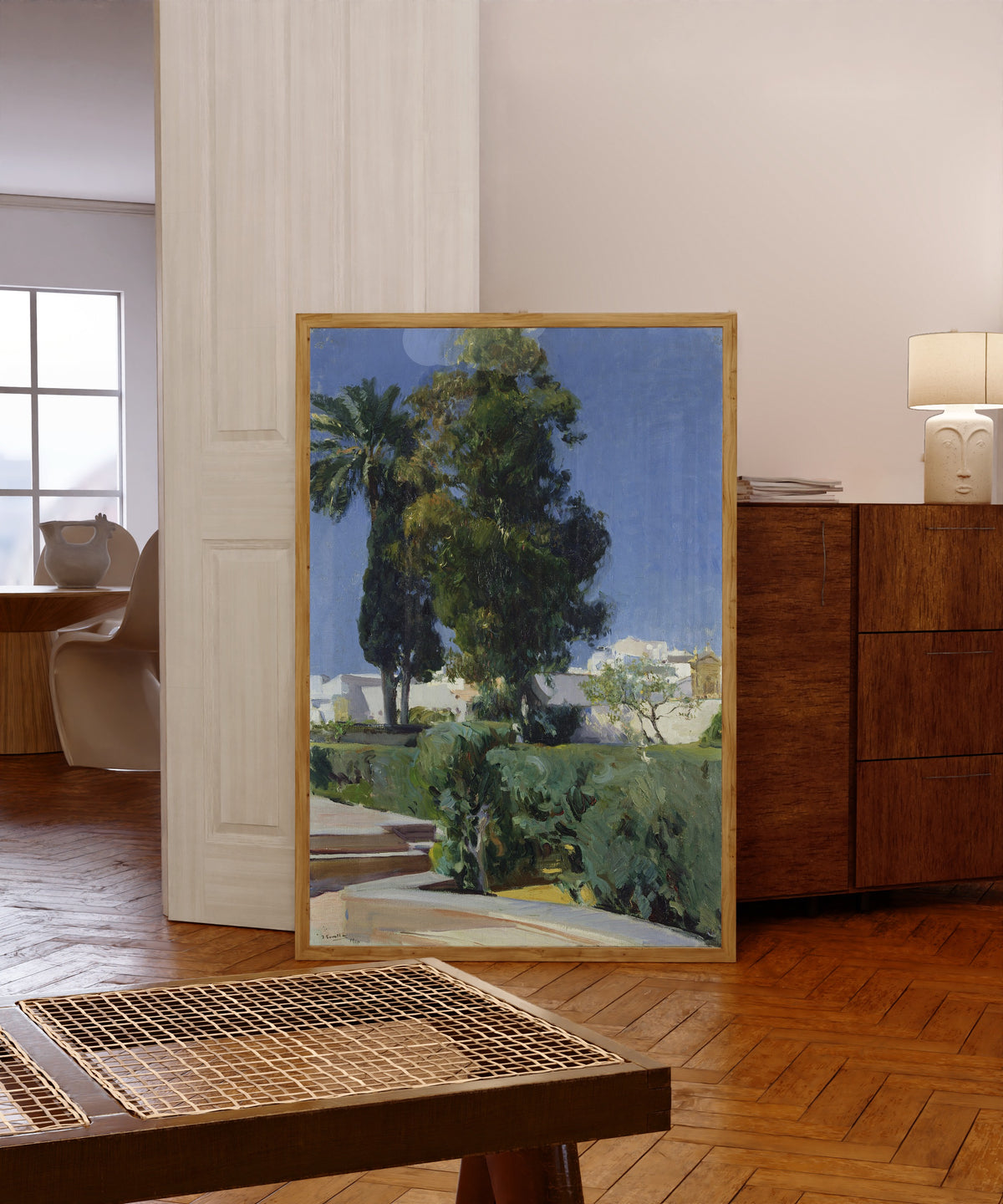 Framed art print of Gardens of the Alcázar, Seville by Joaquín Sorolla, in a light wood frame leaning in a warm room with a parquet floor