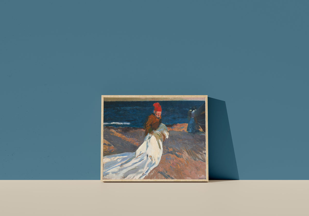 Framed art print of Gathering the Sail, Valencia Beach by Joaquín Sorolla, in a light wood frame leaning on a blue wall