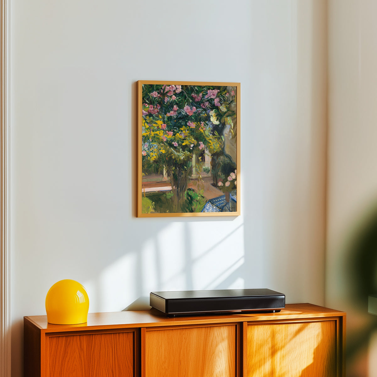 Framed art print of Oleanders in the Courtyard of the Artist's House by Joaquín Sorolla, in a light wood frame on a white wall above an orange sideboard