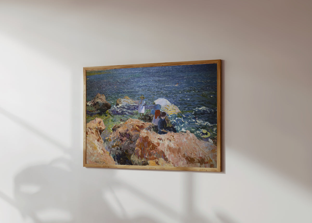 Framed art print of On the Rocks, Jávea by Joaquín Sorolla, in a light wood frame on a sunlit white wall, seen at a slight angle