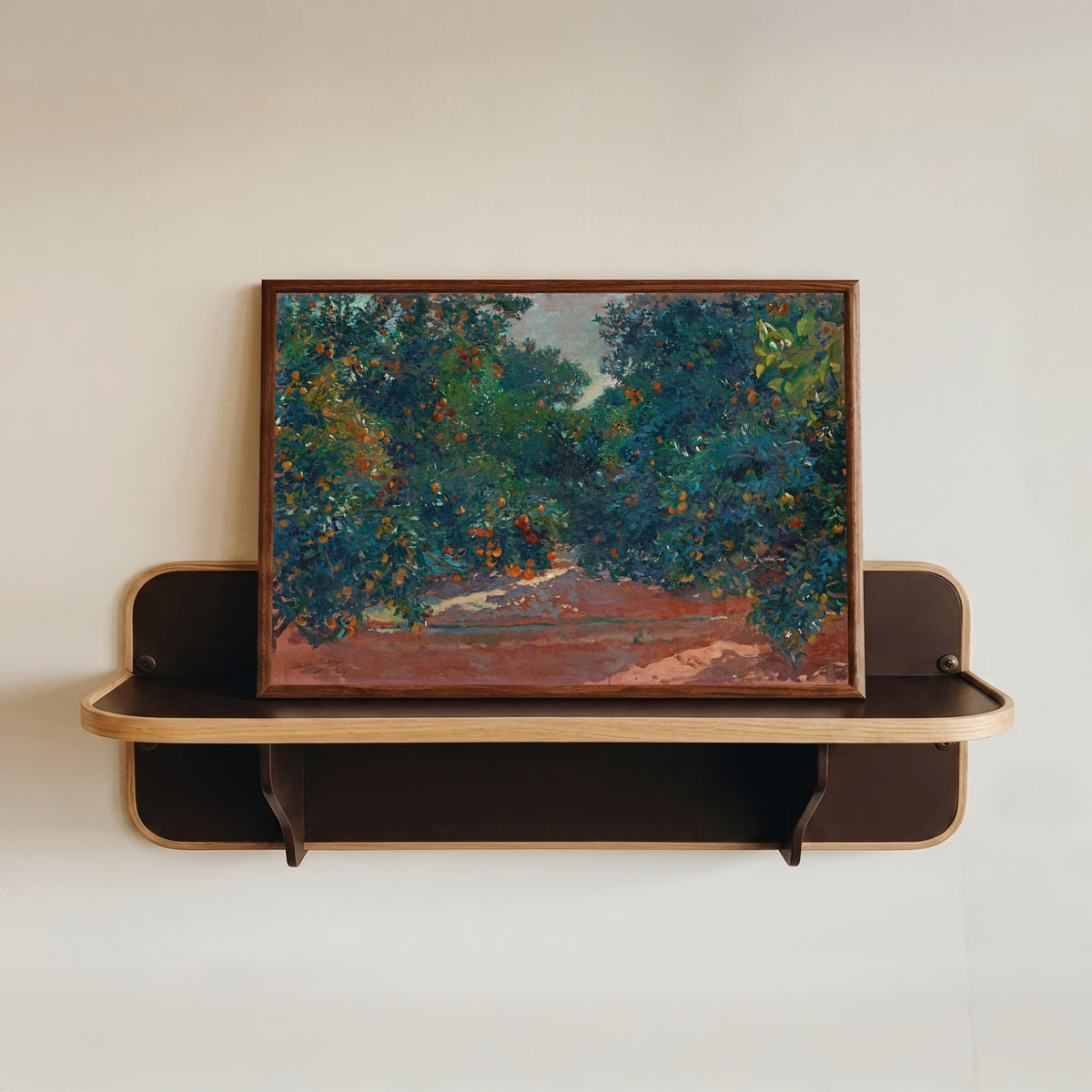 Framed art print of Orange Trees in Alcira by Joaquín Sorolla, in a dark wood frame resting on a wall shelf