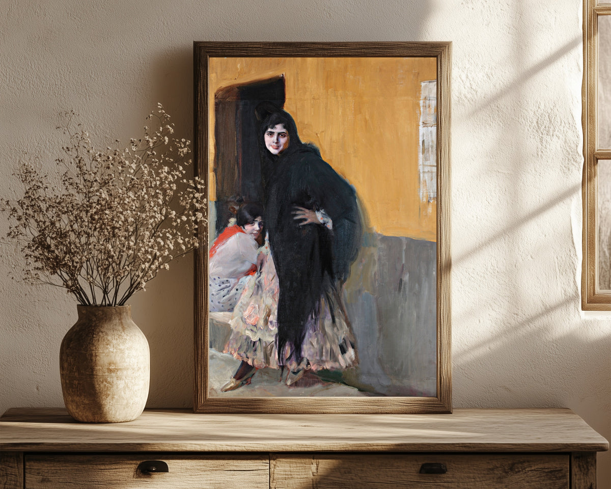 Framed art print of Sevillanas (Ladies of Seville) by Joaquín Sorolla, in a dark wood frame leaning on a rustic console beside dried flowers