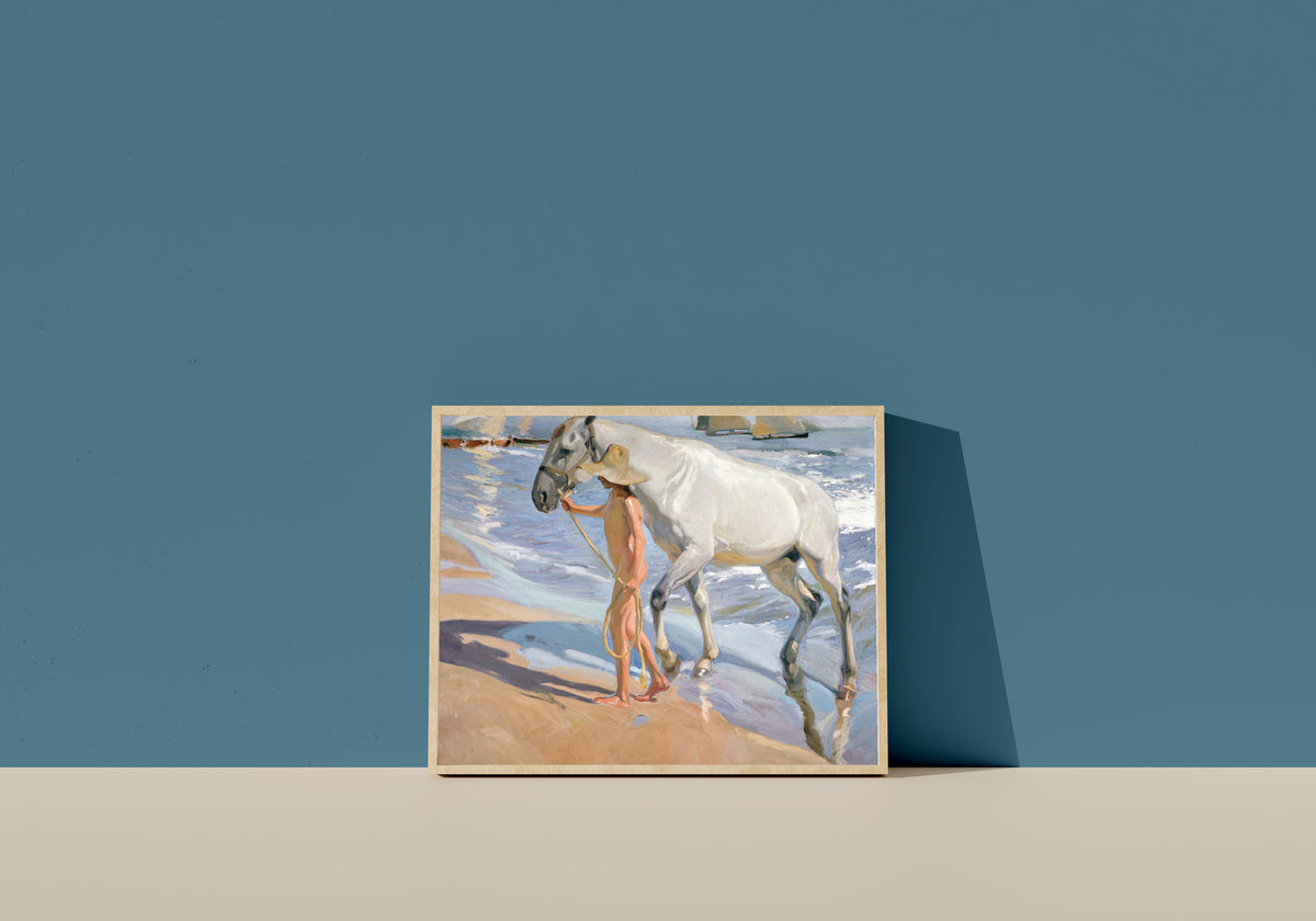 Framed art print of The Horse's Bath by Joaquín Sorolla, in a light wood frame leaning on a blue wall