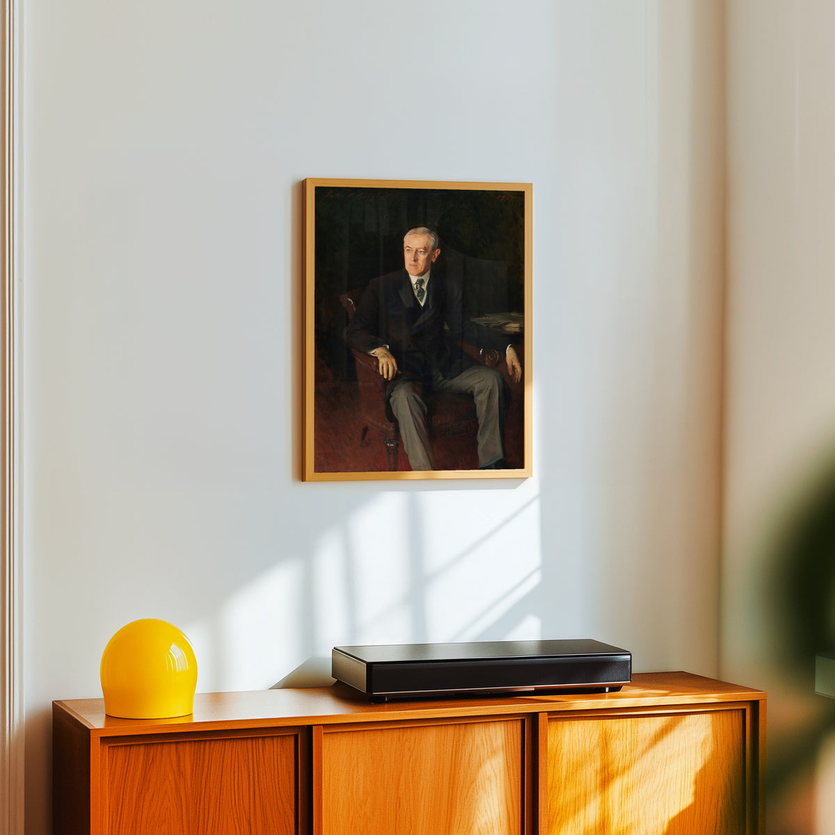 Framed art print of Portrait of Woodrow Wilson by John Singer Sargent, in a light wood frame on a white wall above an orange sideboard