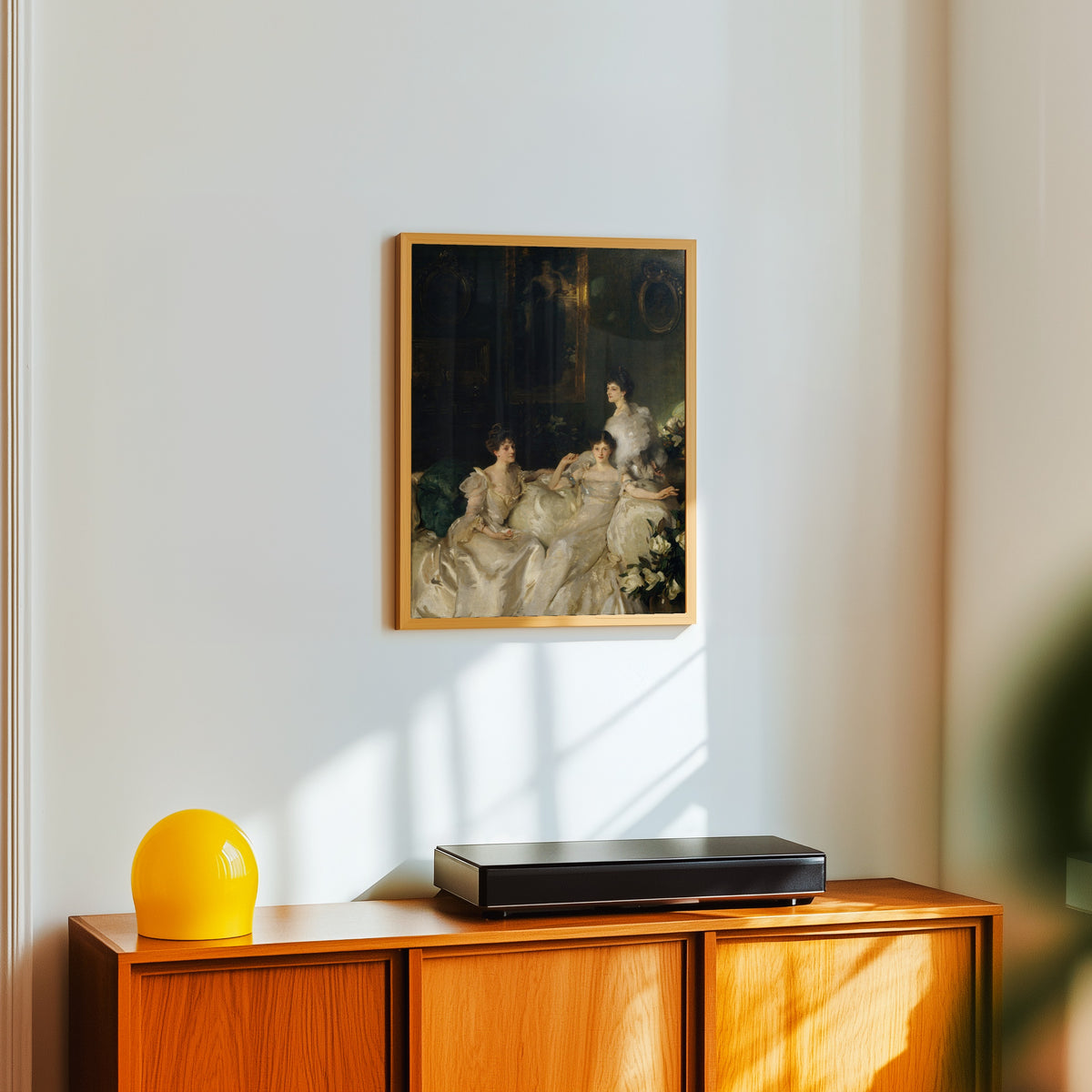 Framed art print of The Wyndham Sisters by John Singer Sargent, in a light wood frame on a white wall above an orange sideboard