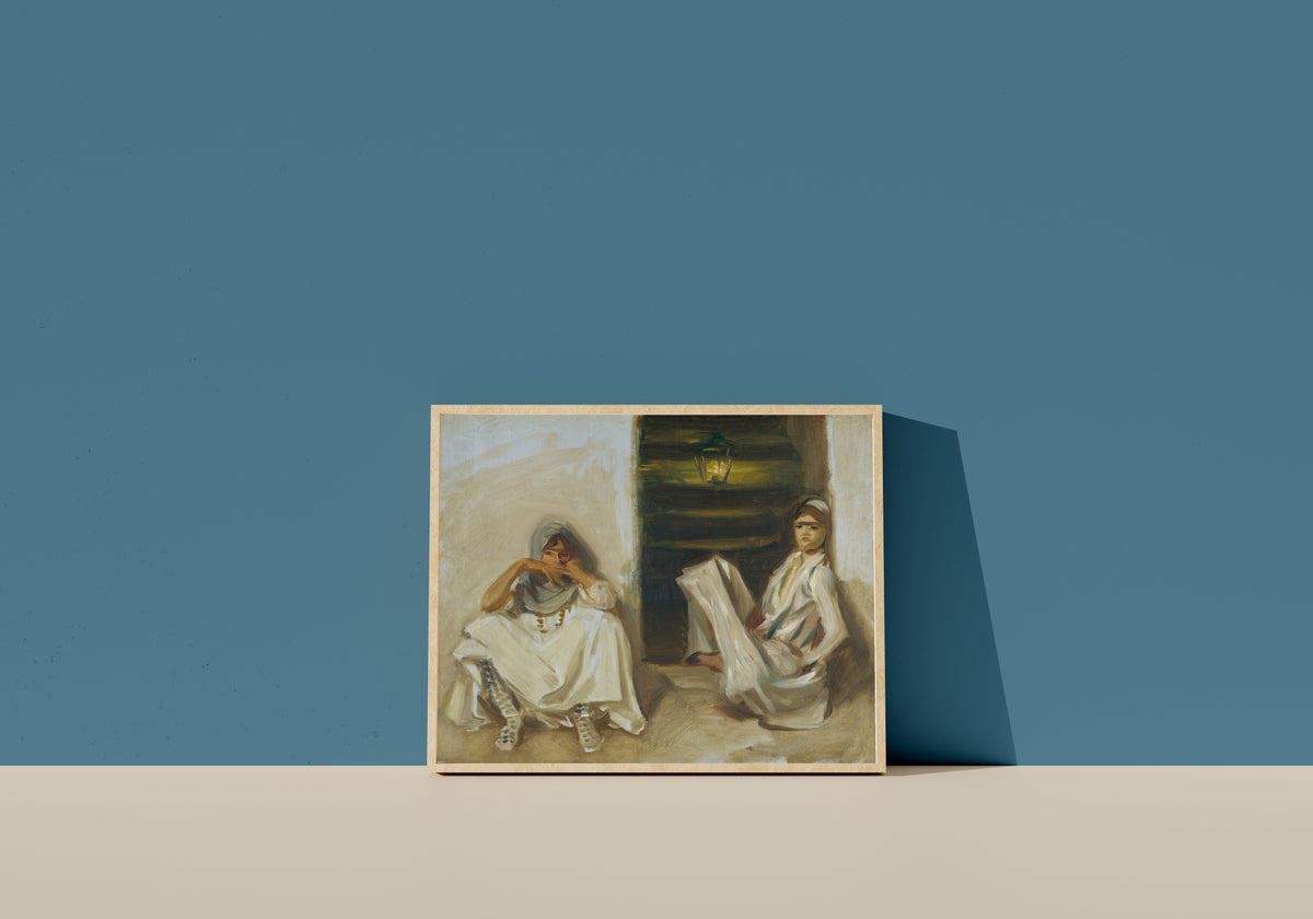 Framed art print of Two Arab Women by John Singer Sargent, in a light wood frame leaning on a blue wall