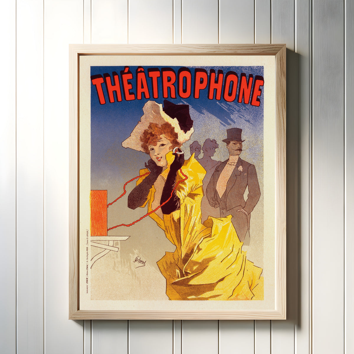 Framed art print of Théâtrophone by Jules Chéret, in a light wood frame on a white panelled wall