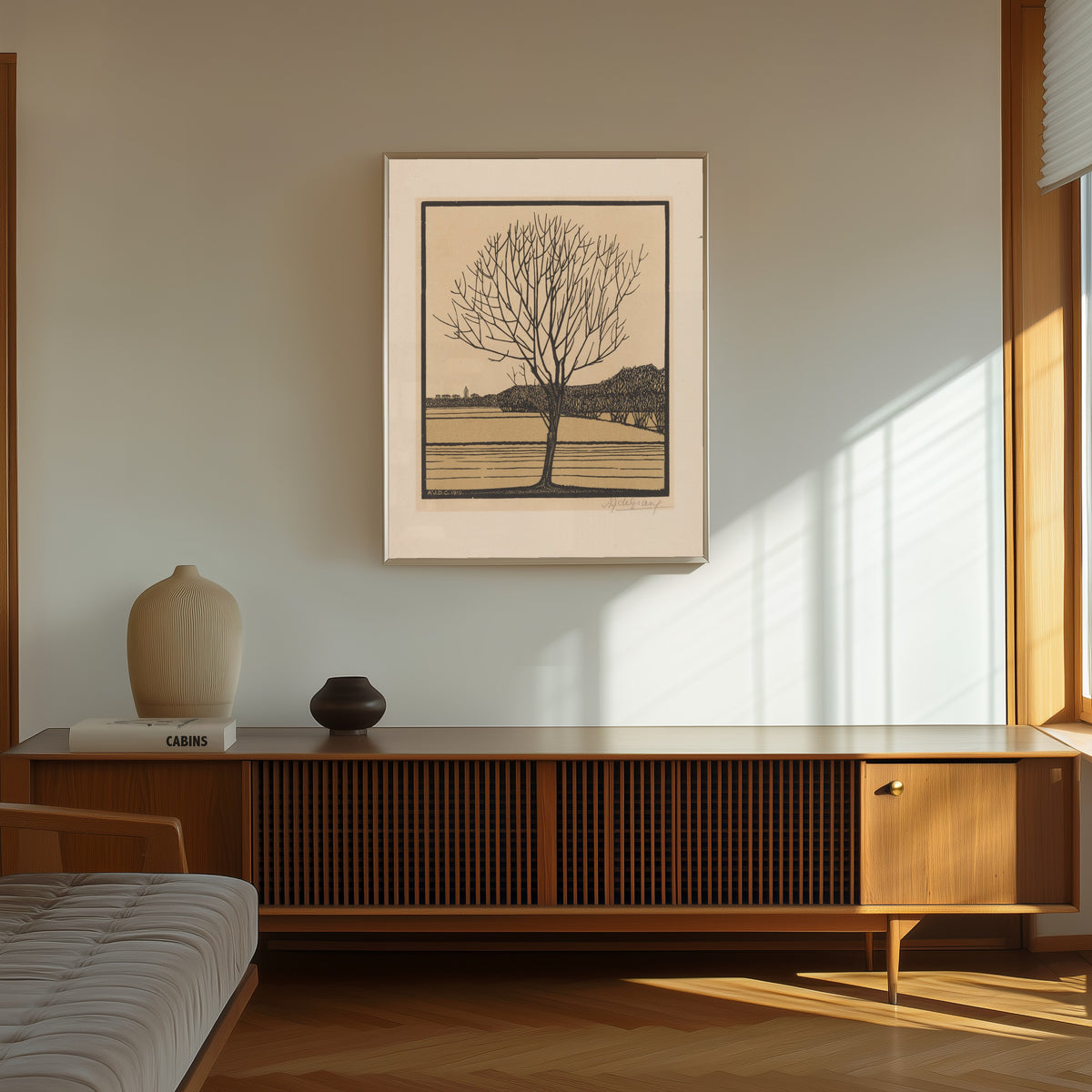 Framed art print of Bare Tree by Water by Julie de Graag, in a thin light frame on a sunlit wall above a wooden sideboard