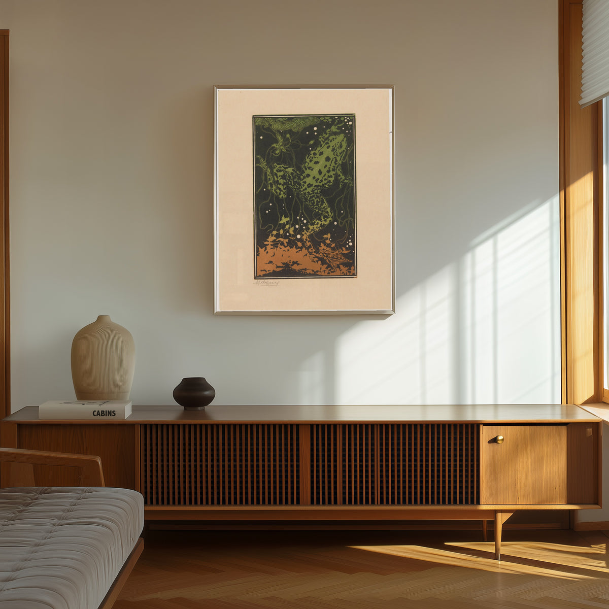 Framed art print of Swimming Frog by Julie de Graag, in a thin light frame on a sunlit wall above a wooden sideboard