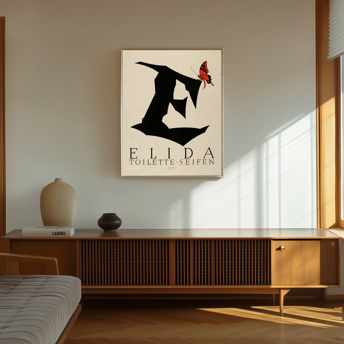 Framed art print of Elida Toilette-Seifen by Julius Klinger, in a thin light frame on a sunlit wall above a wooden sideboard