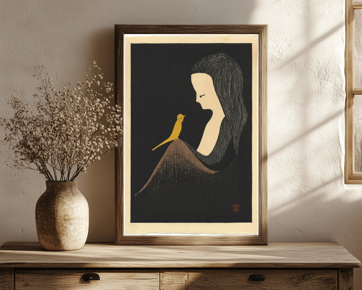 Framed art print of Girl with Yellow Bird by Kaoru Kawano, in a dark wood frame leaning on a rustic console beside dried flowers