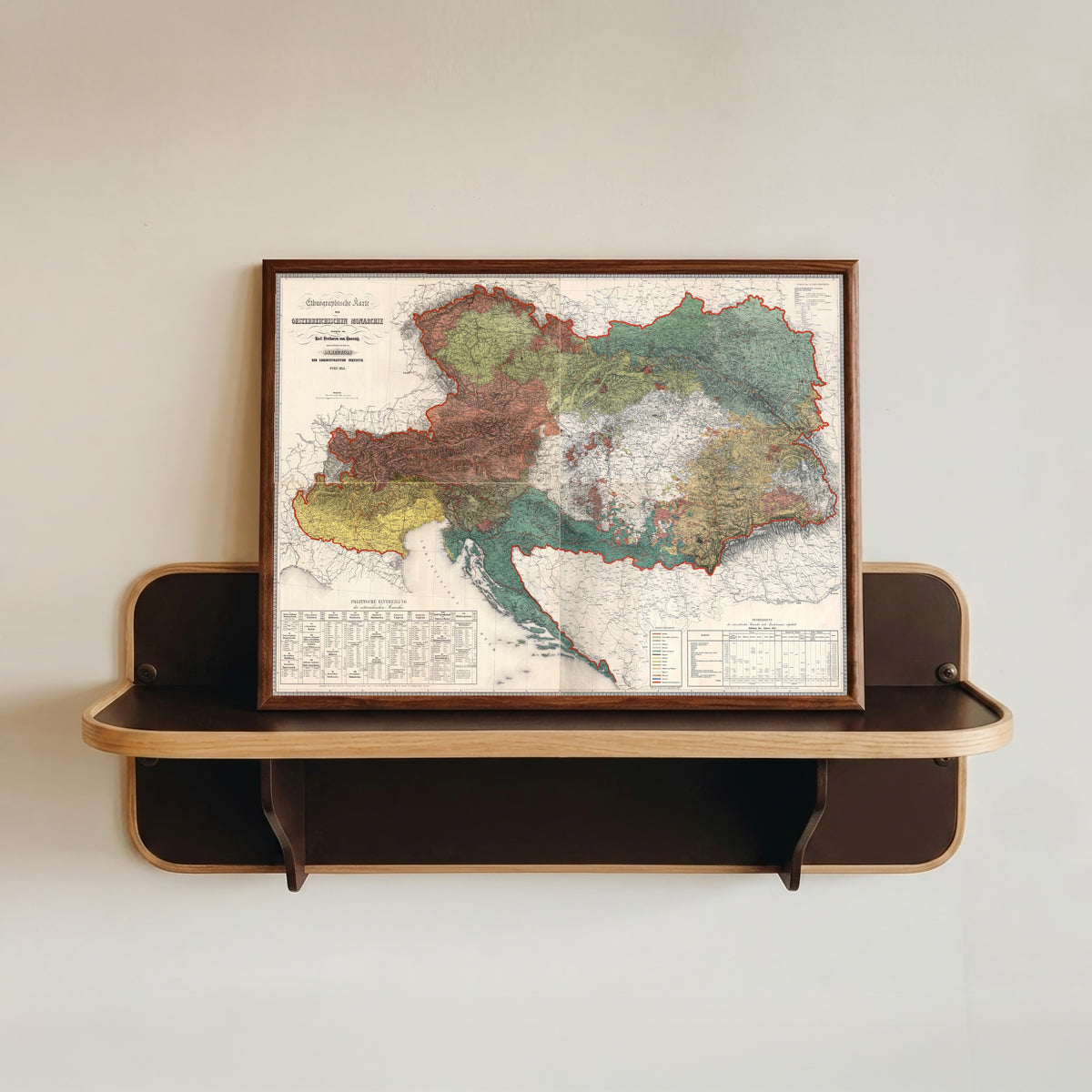 Framed art print of Ethnographic Map of the Austrian Monarchy by Karl von Czoernig, in a dark wood frame resting on a wall shelf