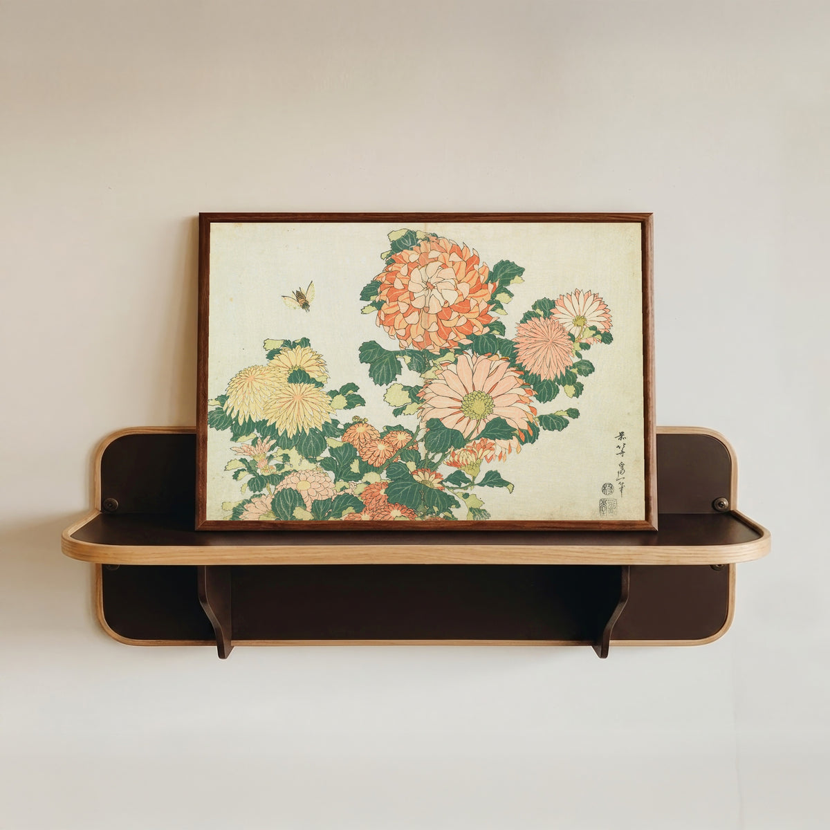 Framed art print of Large Flowers: Chrysanthemums and Horsefly by Katsushika Hokusai, in a dark wood frame resting on a wall shelf