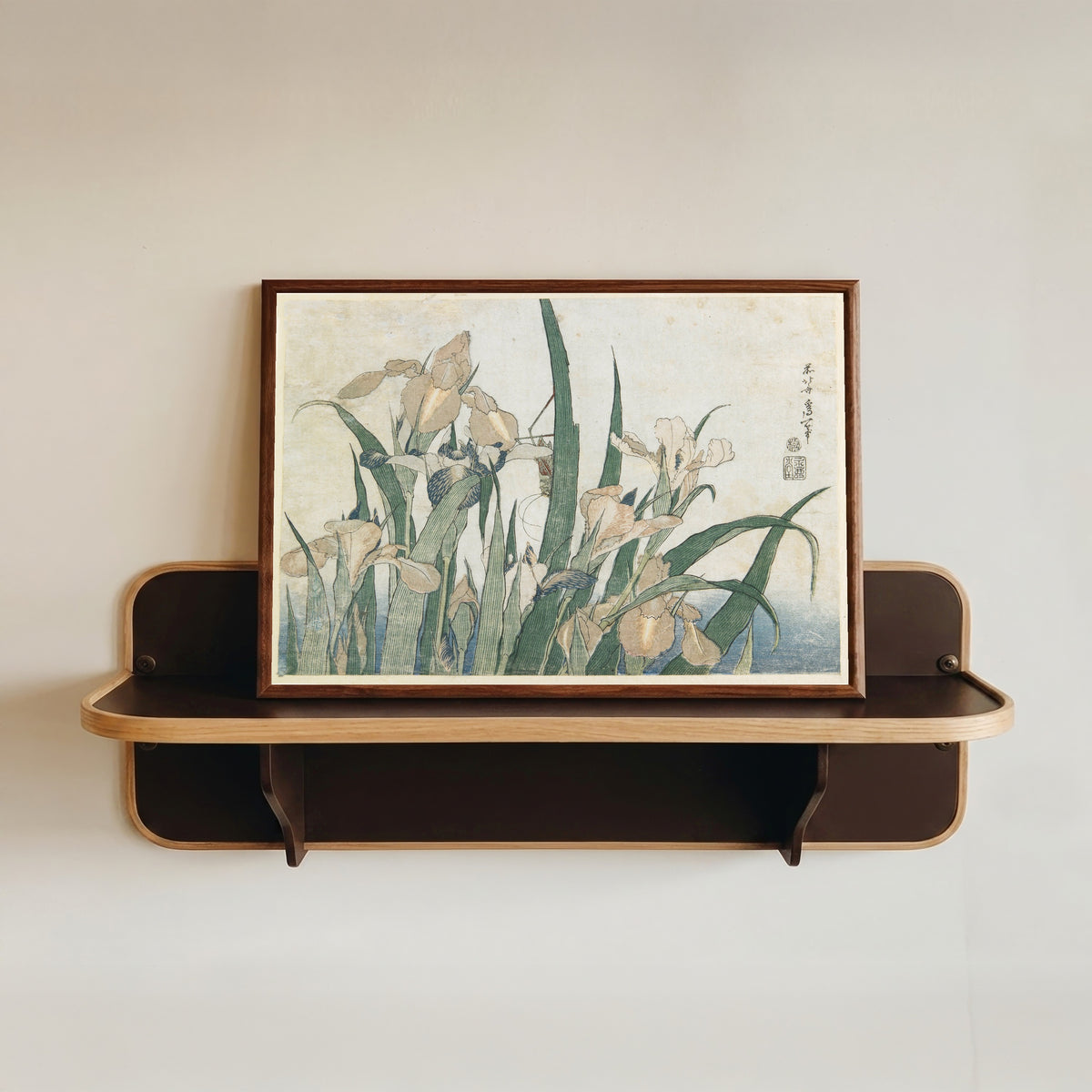 Framed art print of Large Flowers: Irises and Grasshopper by Katsushika Hokusai, in a dark wood frame resting on a wall shelf