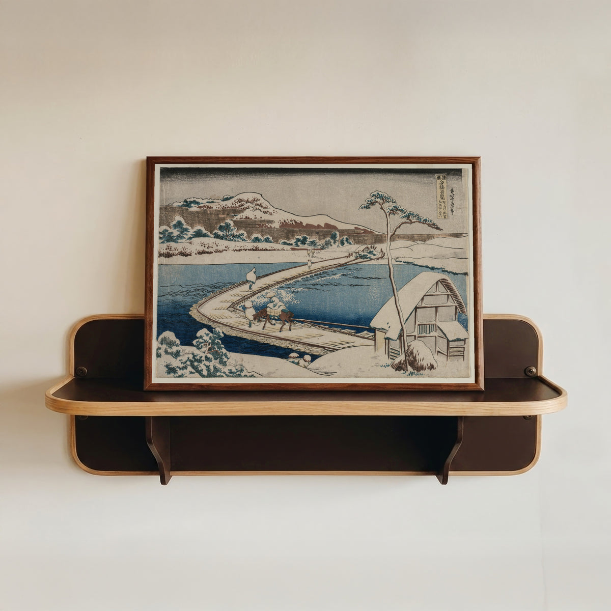 Framed art print of Remarkable Views of Bridges in Various Provinces: An Ancient Picture… by Katsushika Hokusai, in a dark wood frame resting on a wall shelf