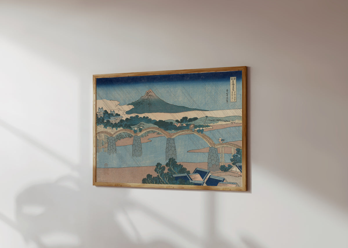 Framed art print of Remarkable Views of Bridges in Various… by Katsushika Hokusai, in a light wood frame on a sunlit white wall, seen at a slight angle