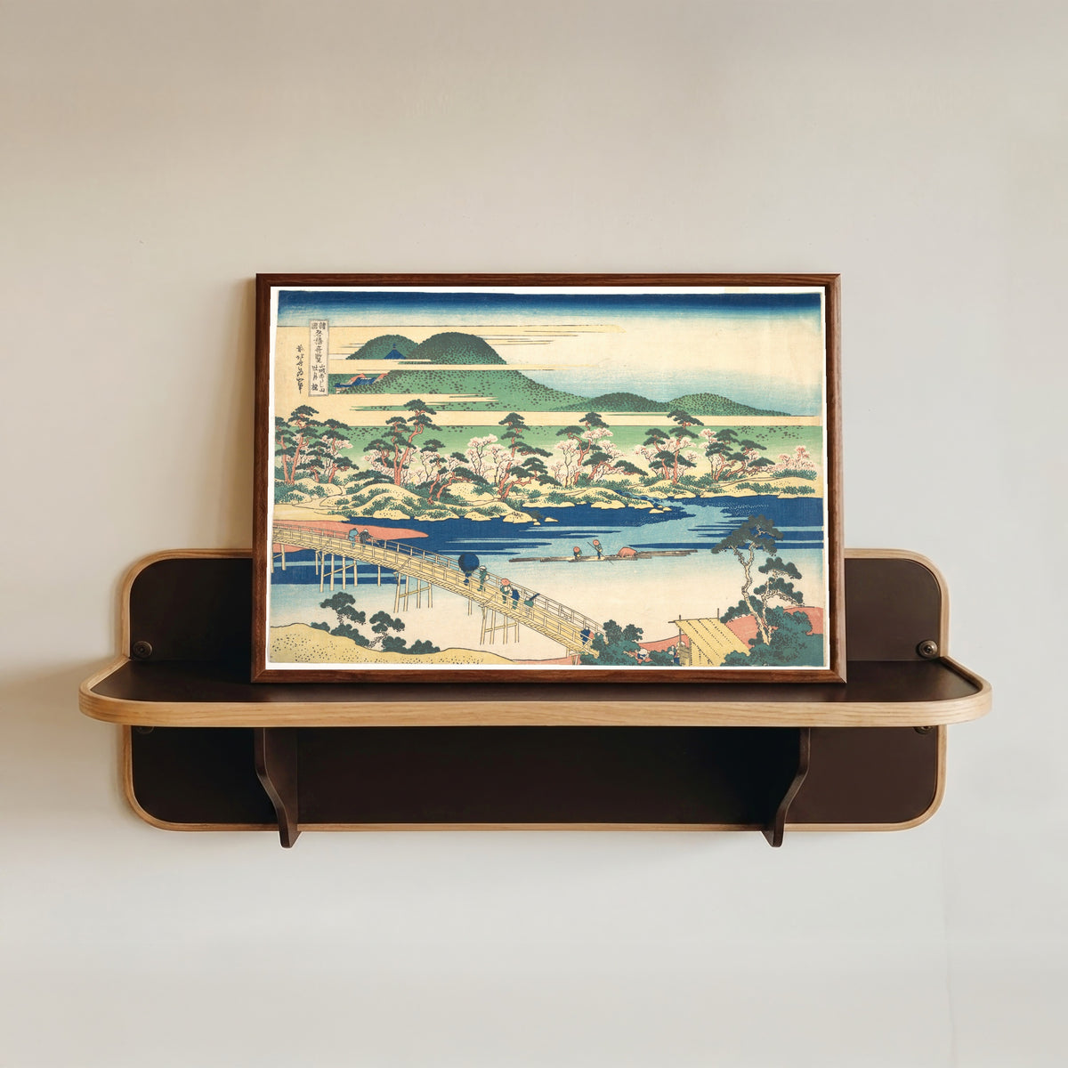 Framed art print of Remarkable Views of Bridges in Various Provinces: Togetsu Bridge at… by Katsushika Hokusai, in a dark wood frame resting on a wall shelf