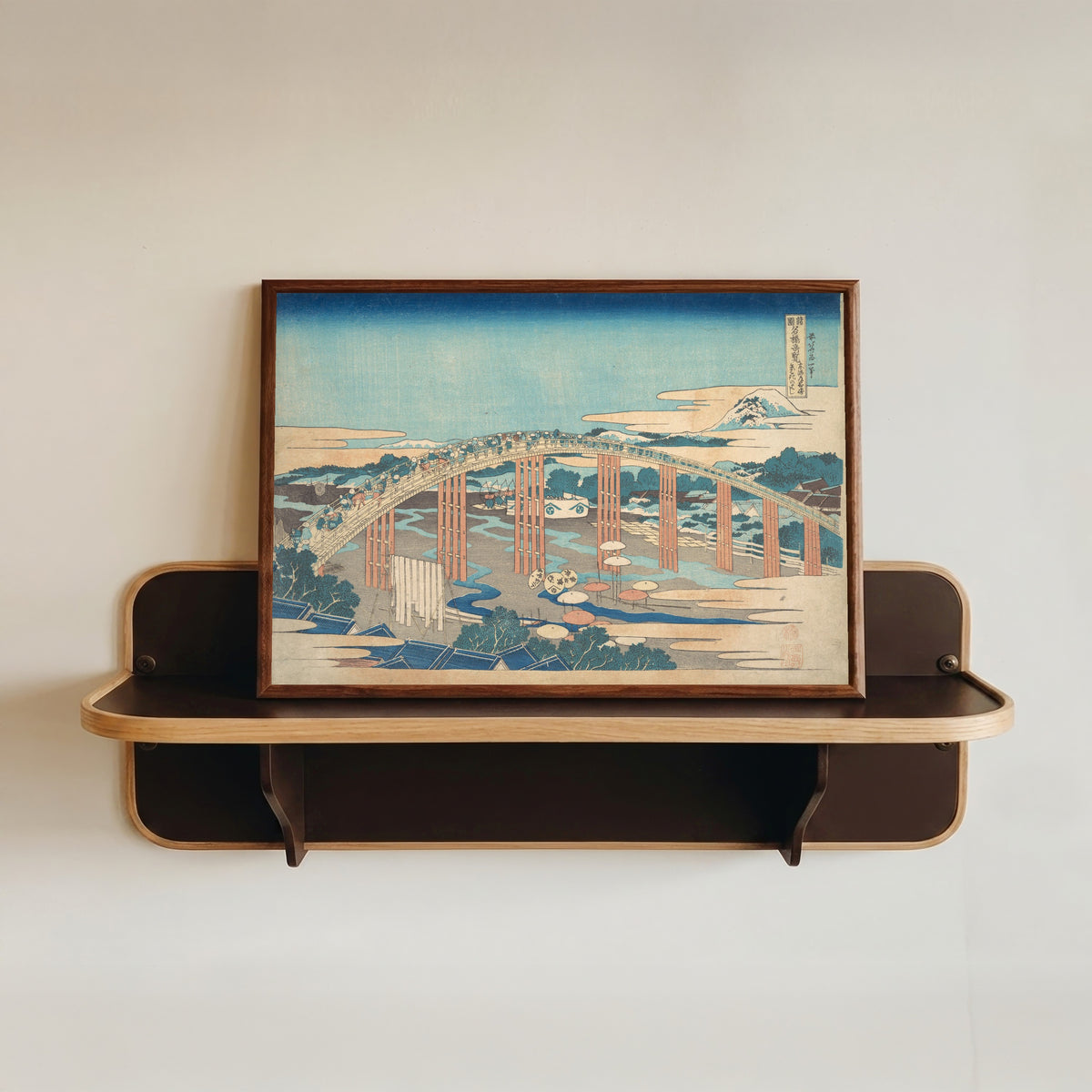 Framed art print of Remarkable Views of Bridges in Various Provinces: Yahagi Bridge at… by Katsushika Hokusai, in a dark wood frame resting on a wall shelf