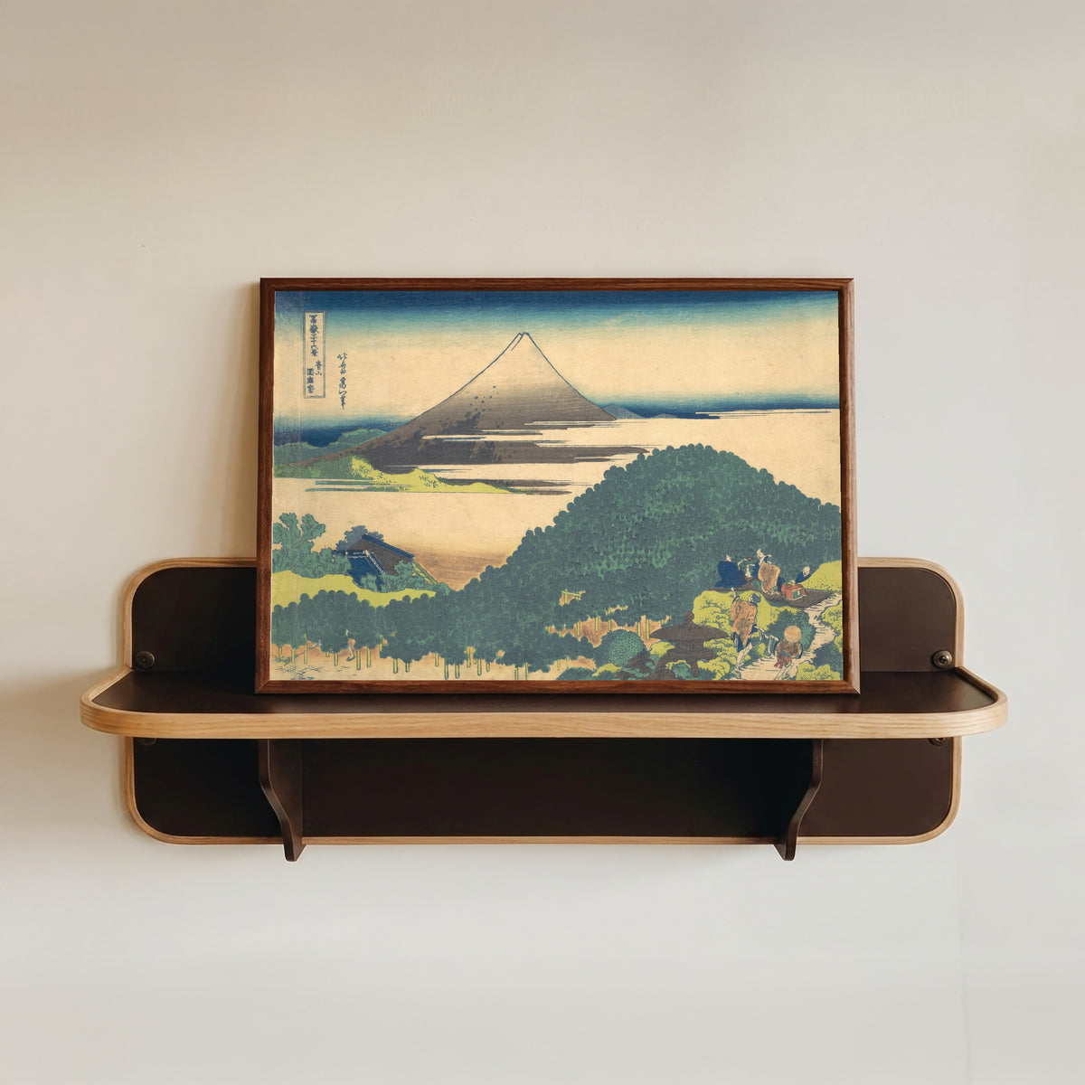 Framed art print of Thirty-six Views of Mount Fuji: Cushion Pine at Aoyama by Katsushika Hokusai, in a dark wood frame resting on a wall shelf