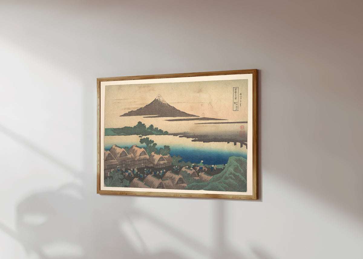 Framed art print of Thirty-six Views of Mount Fuji: Dawn at Isawa… by Katsushika Hokusai, in a light wood frame on a sunlit white wall, seen at a slight angle