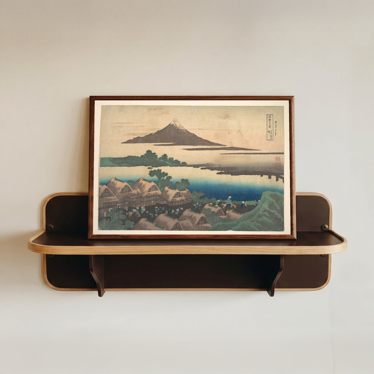 Framed art print of Thirty-six Views of Mount Fuji: Dawn at Isawa in Kai Province by Katsushika Hokusai, in a dark wood frame resting on a wall shelf