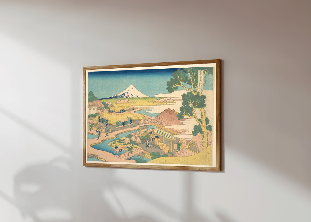 Framed art print of Thirty-six Views of Mount Fuji: Fuji from the… by Katsushika Hokusai, in a light wood frame on a sunlit white wall, seen at a slight angle