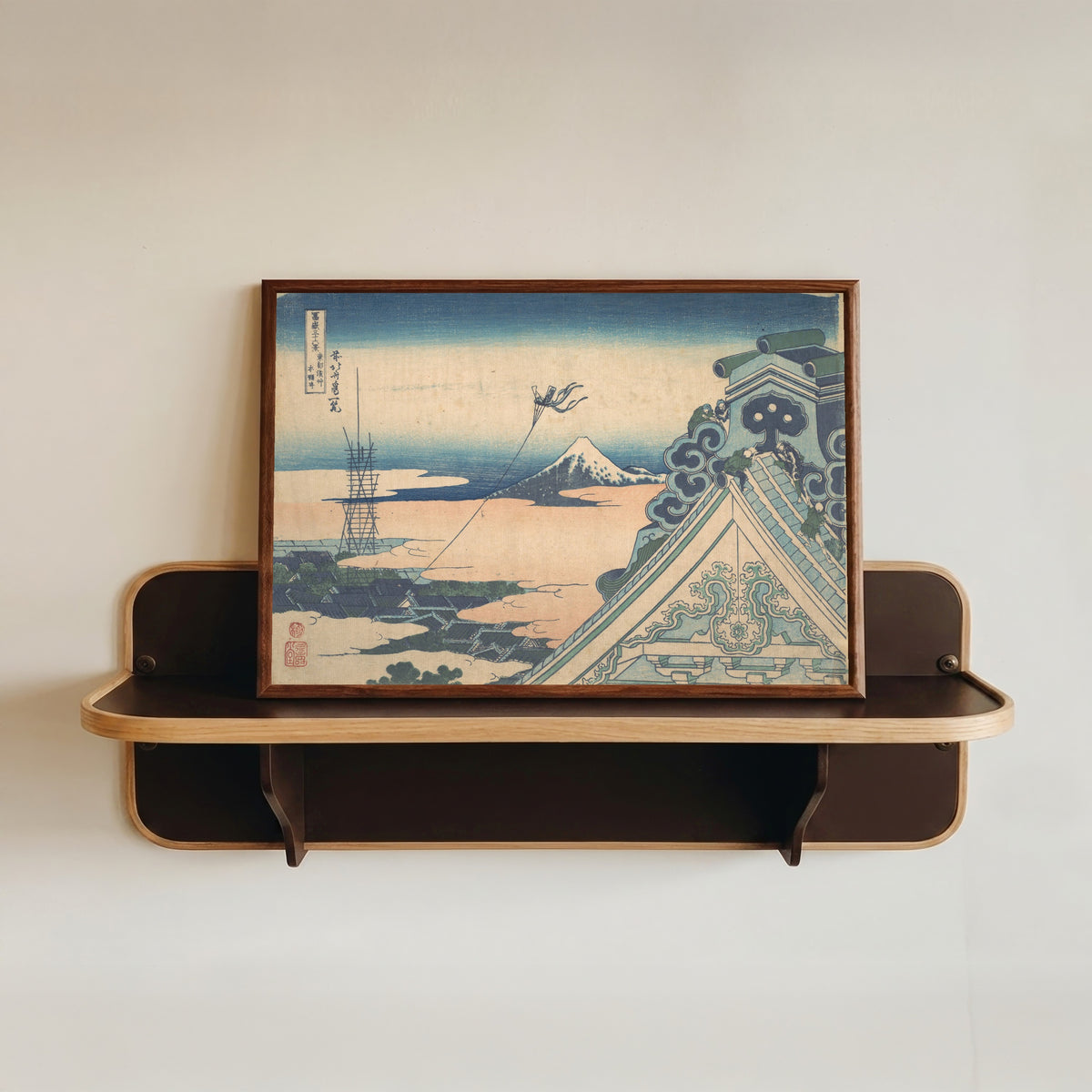 Framed art print of Thirty-six Views of Mount Fuji: Honganji at Asakusa in Edo by Katsushika Hokusai, in a dark wood frame resting on a wall shelf