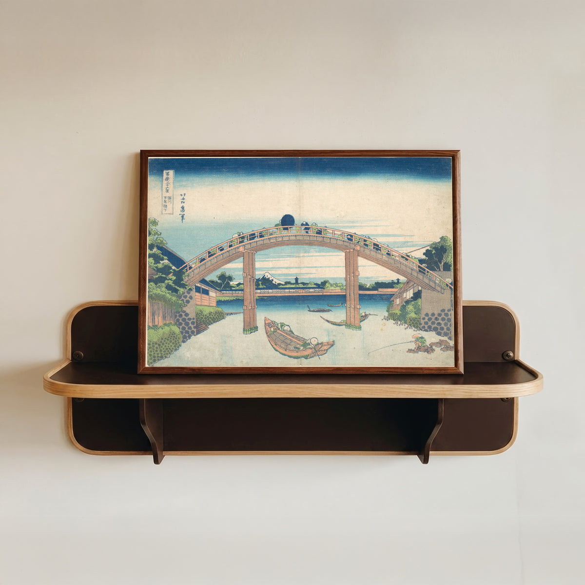 Framed art print of Thirty-six Views of Mount Fuji: Under the Mannen Bridge at Fukagawa by Katsushika Hokusai, in a dark wood frame resting on a wall shelf
