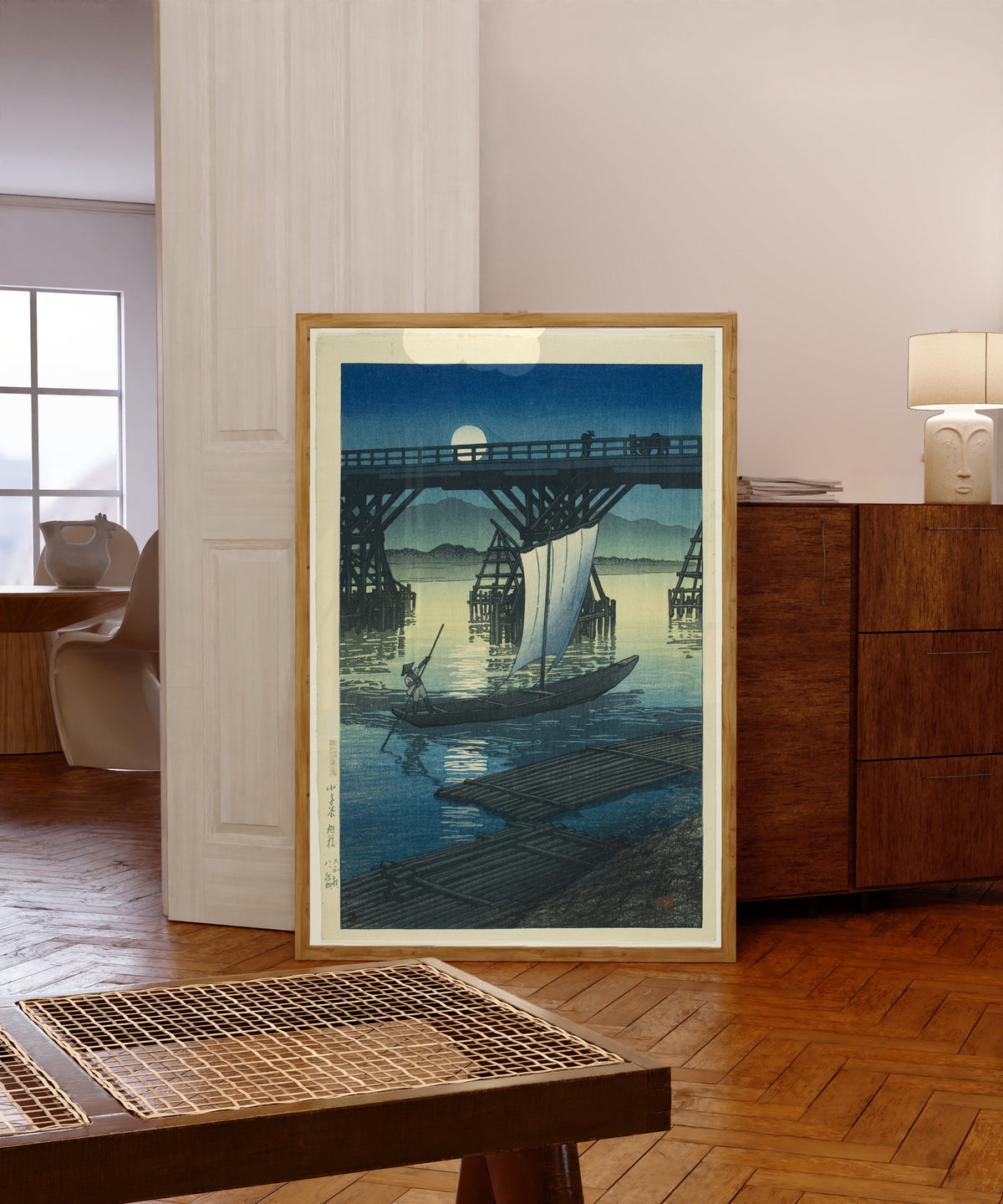 Framed art print of Asahi Bridge by Kawase Hasui, in a light wood frame leaning in a warm room with a parquet floor