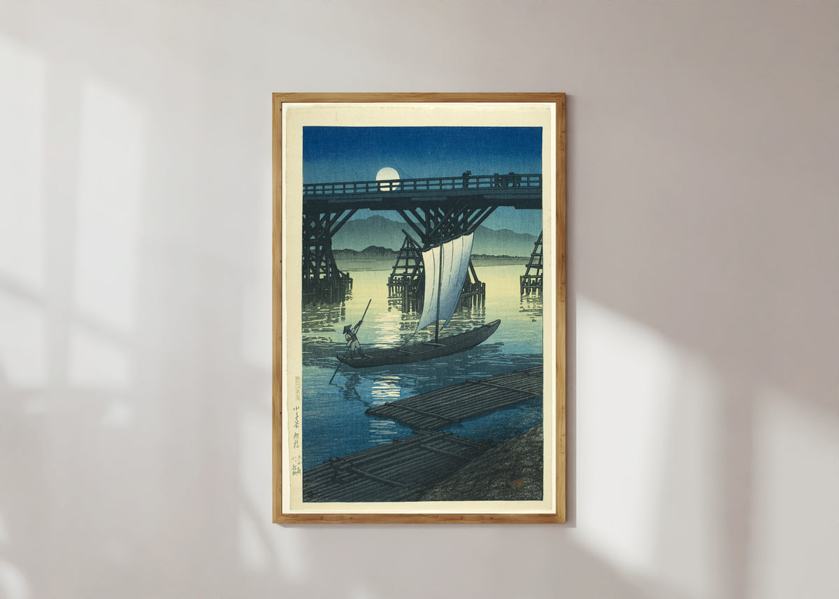 Framed art print of Asahi Bridge by Kawase Hasui, in a light wood frame on a sunlit white wall