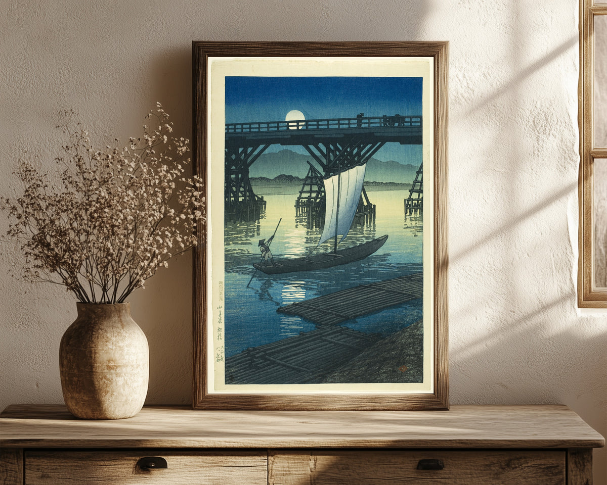 Framed art print of Asahi Bridge by Kawase Hasui, in a dark wood frame leaning on a rustic console beside dried flowers