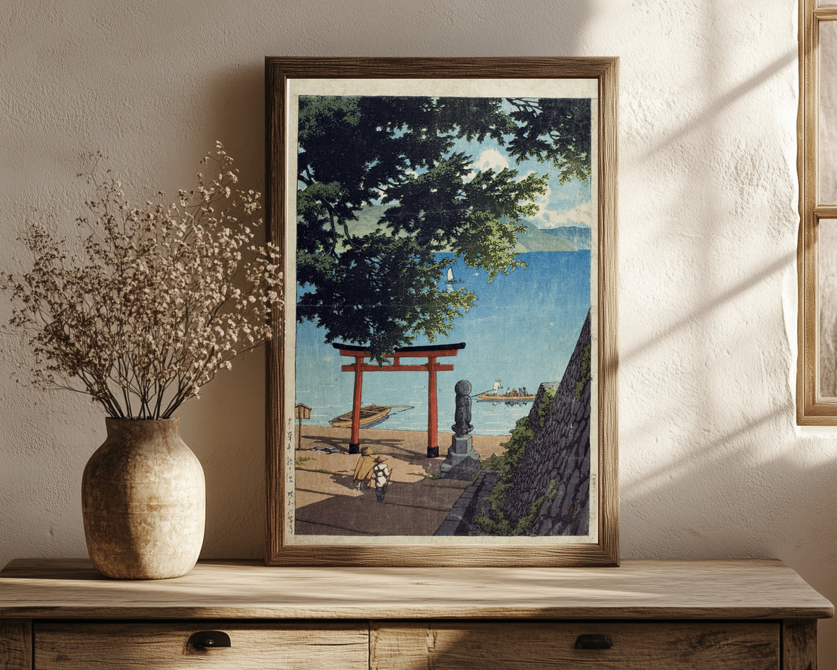 Framed art print of Chuzenji Lake, Utagahama by Kawase Hasui, in a dark wood frame leaning on a rustic console beside dried flowers