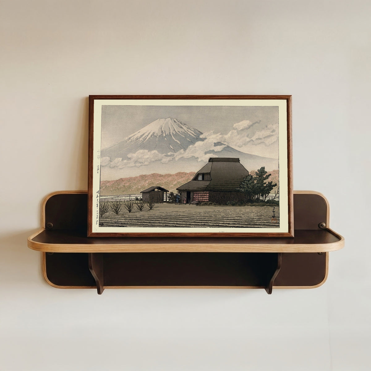 Framed art print of Countryside at Narusawa by Kawase Hasui, in a dark wood frame resting on a wall shelf